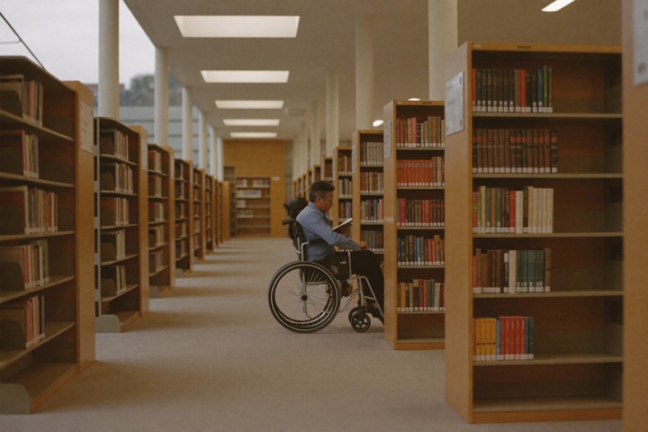 Rolstoelgebruiker zoekt een boek uit in een ruime, moderne bibliotheek