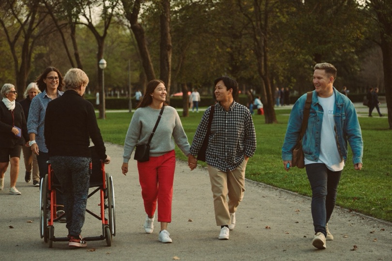 Een diverse groep mensen, onder wie een rolstoelgebruiker, wandelt samen door een park