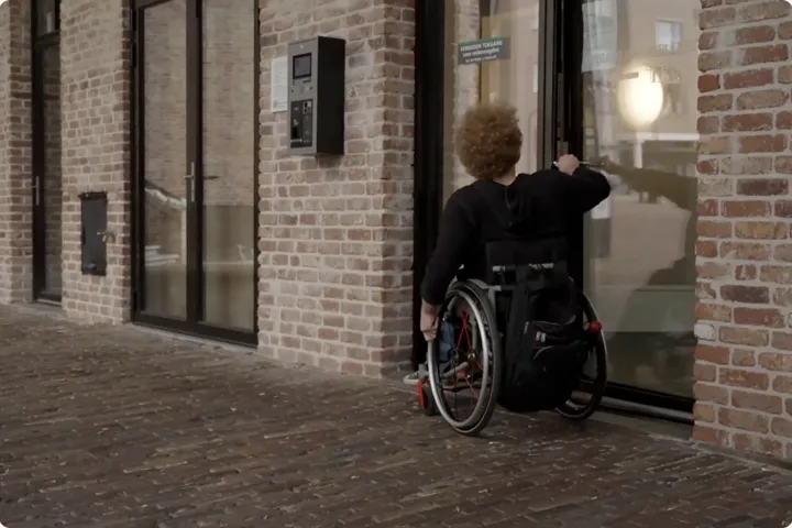 Rolstoelgebruiker trekt een zware deur bij de ingang van een parkeergarage open